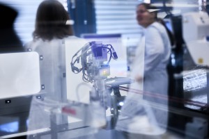 Spiegelung eines Laborger&auml;ts in einer Glasscheibe mit unscharfen Personen